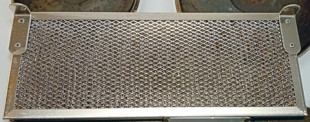 Bulaşık makinesinden sökülmüş metal filtre, kirli ve yemek artıkları yapışmış halde gösteriliyor
