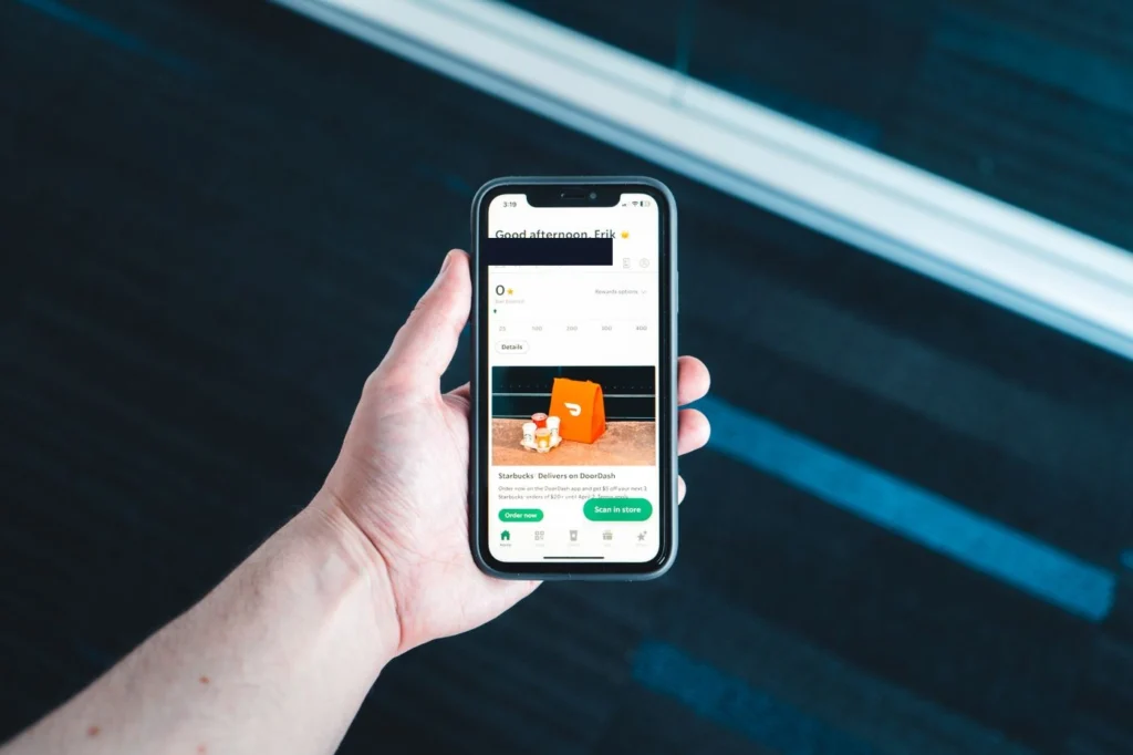 Bir kişinin elinde tuttuğu akıllı telefon ekranında, turuncu renkli bir ürün görseli ve altında yeşil renkte işlem butonları (muhtemelen iade/sorun bildirme seçenekleri) görülmektedir.