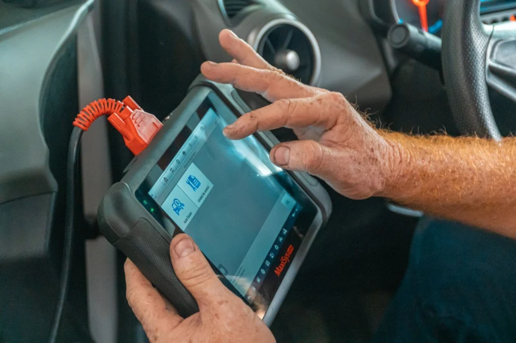 Bir kişinin araç içinde OBD tarayıcı cihazını elle tutarak tablet benzeri ekranda okumalar yapıyor görüntüsü