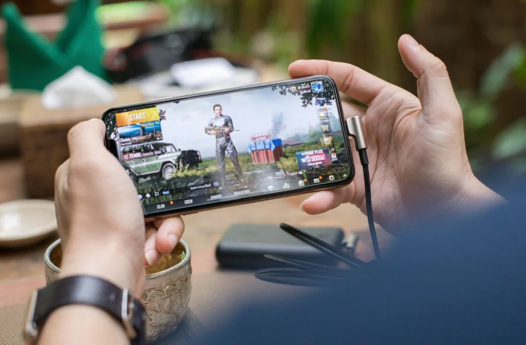 Elde tutulan telefonda PUBG Mobile oyun ekranı görünüyor, ancak Stil/Gölge ayarları menüsü net olarak görünmüyor